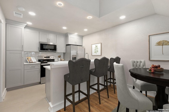 kitchen featuring a kitchen breakfast bar, vaulted ceiling, appliances with stainless steel finishes, light hardwood / wood-style flooring, and tasteful backsplash