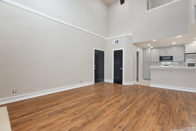 unfurnished living room with light hardwood / wood-style flooring and a towering ceiling