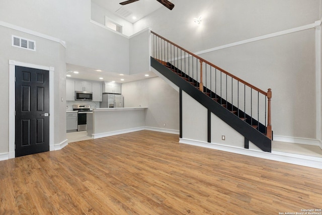 unfurnished living room with ceiling fan, light hardwood / wood-style flooring, and a towering ceiling