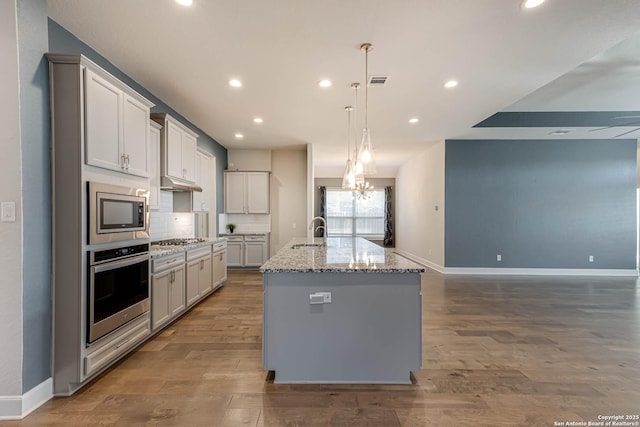 kitchen featuring light stone countertops, appliances with stainless steel finishes, a kitchen island with sink, sink, and an inviting chandelier