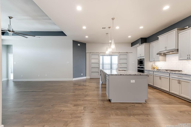 kitchen featuring a kitchen island with sink, light hardwood / wood-style flooring, ceiling fan, light stone countertops, and white cabinetry