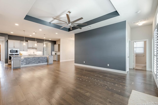 unfurnished living room featuring ceiling fan, sink, dark wood-type flooring, and a tray ceiling