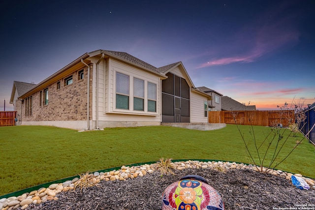 back house at dusk featuring a lawn and a sunroom