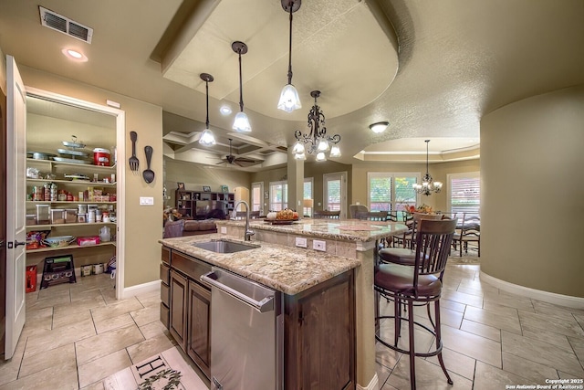 kitchen with light stone counters, stainless steel dishwasher, a kitchen island with sink, sink, and decorative light fixtures