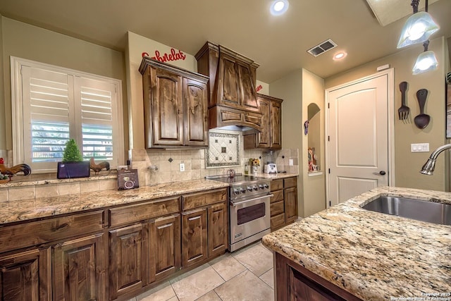 kitchen with backsplash, light stone counters, stainless steel range, custom range hood, and sink