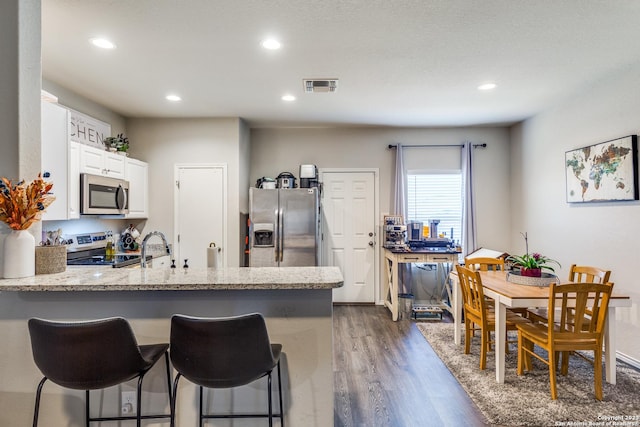 kitchen featuring a kitchen bar, appliances with stainless steel finishes, kitchen peninsula, dark wood-type flooring, and white cabinets