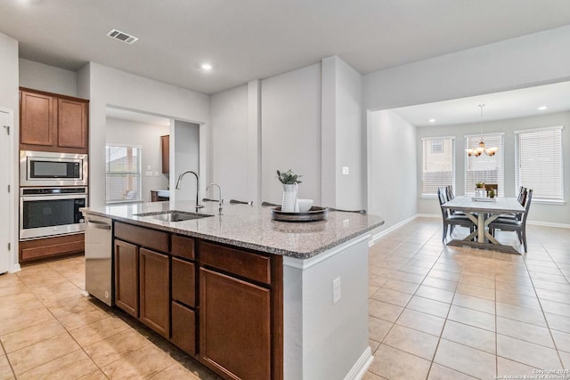 kitchen featuring light stone counters, stainless steel appliances, a kitchen island with sink, sink, and pendant lighting