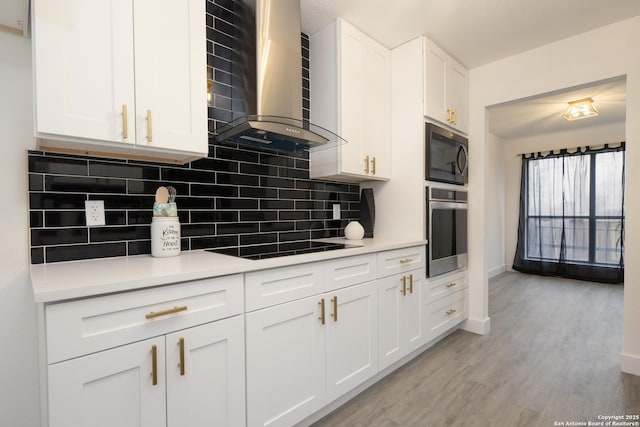 kitchen with built in microwave, wall chimney exhaust hood, backsplash, oven, and white cabinets