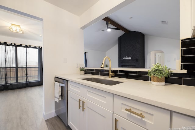 kitchen with white cabinets, lofted ceiling with beams, sink, stainless steel dishwasher, and light wood-type flooring