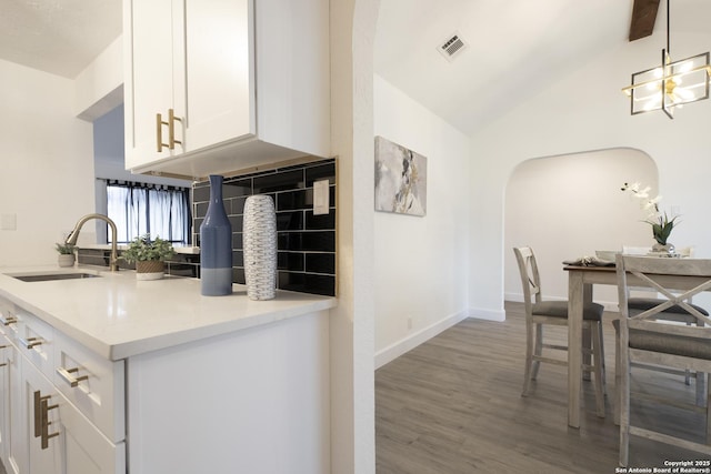 kitchen featuring vaulted ceiling, sink, wood-type flooring, pendant lighting, and white cabinets