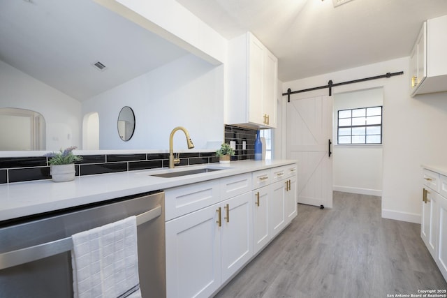 kitchen featuring a barn door, white cabinetry, sink, and stainless steel dishwasher