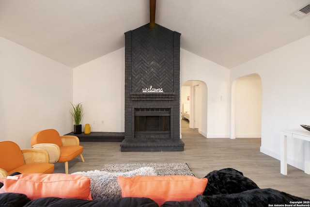 living room featuring a brick fireplace, vaulted ceiling with beams, and light hardwood / wood-style flooring