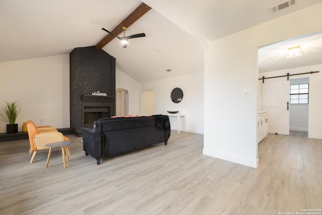 living room featuring ceiling fan, a barn door, vaulted ceiling with beams, a fireplace, and light wood-type flooring