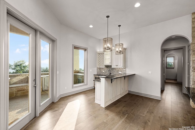 kitchen with kitchen peninsula, tasteful backsplash, hardwood / wood-style floors, white cabinetry, and hanging light fixtures