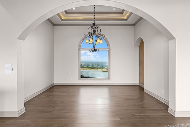 interior space with a tray ceiling, dark wood-type flooring, ornamental molding, and an inviting chandelier