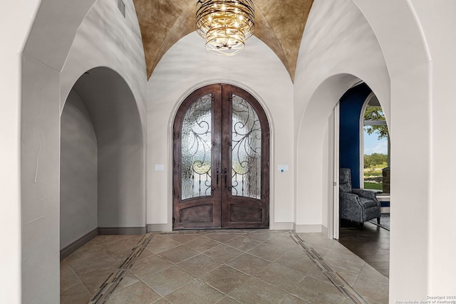 foyer entrance featuring a chandelier, french doors, vaulted ceiling, and brick ceiling