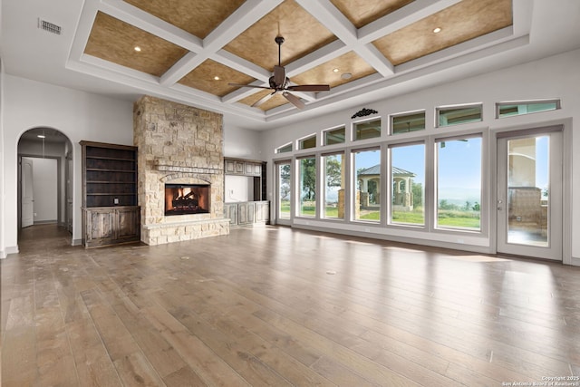 unfurnished living room featuring beamed ceiling, a stone fireplace, a towering ceiling, and coffered ceiling