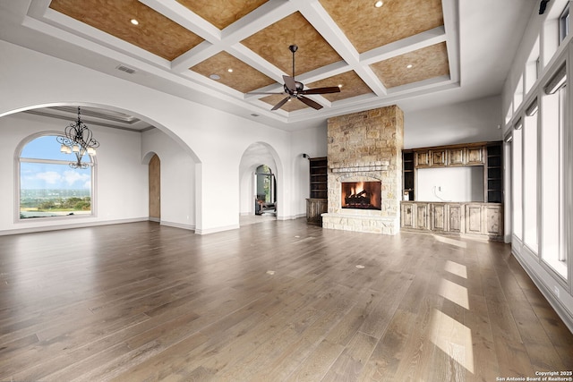 unfurnished living room with a high ceiling, coffered ceiling, ceiling fan with notable chandelier, a stone fireplace, and beamed ceiling