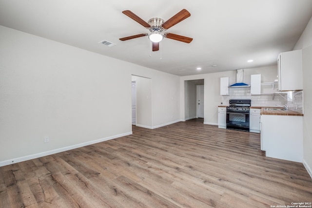 kitchen with white cabinets, black range with gas stovetop, wall chimney range hood, light hardwood / wood-style flooring, and decorative backsplash