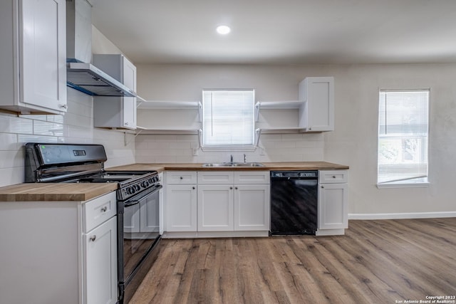 kitchen featuring black appliances, wall chimney range hood, light wood-type flooring, butcher block countertops, and white cabinetry