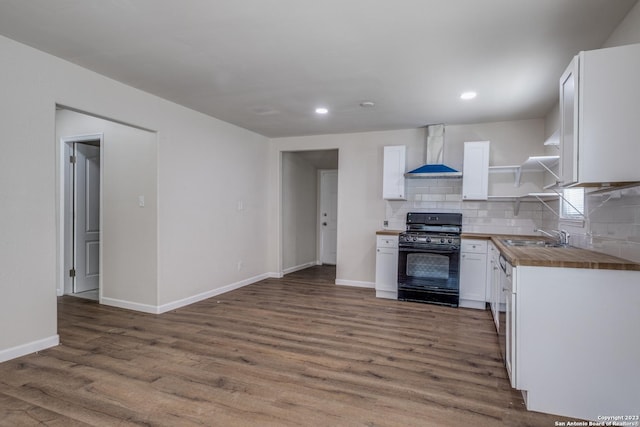 kitchen with black range with gas stovetop, wall chimney exhaust hood, decorative backsplash, butcher block countertops, and white cabinetry