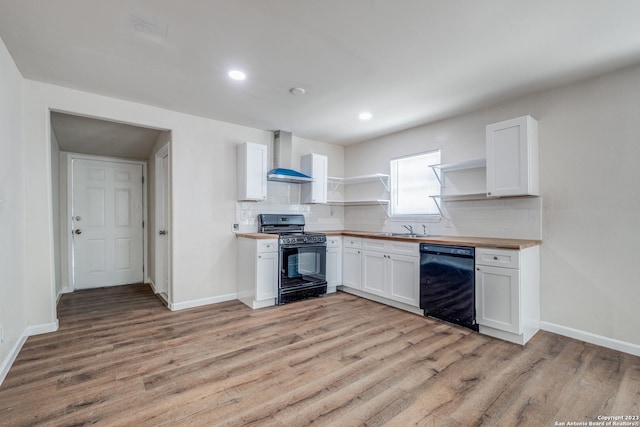 kitchen with black appliances, wall chimney range hood, white cabinetry, light hardwood / wood-style floors, and butcher block counters