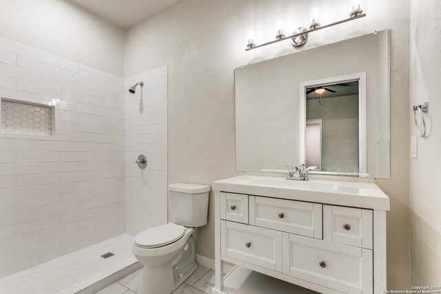 bathroom with a tile shower, ceiling fan, vanity, and toilet