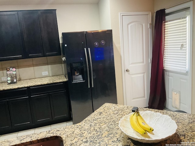 kitchen with backsplash, black fridge, light tile patterned floors, and light stone countertops