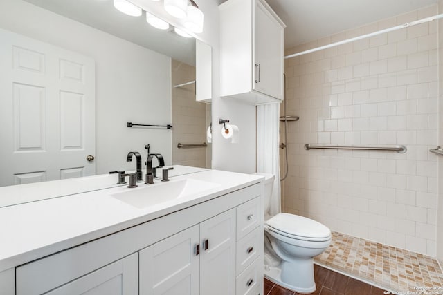 bathroom with tiled shower, vanity, hardwood / wood-style flooring, and toilet