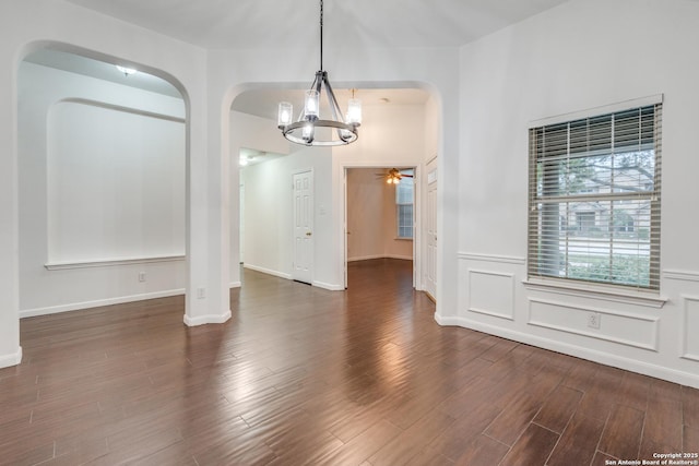 unfurnished dining area featuring ceiling fan with notable chandelier and dark hardwood / wood-style flooring