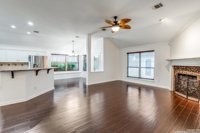 unfurnished living room with ceiling fan with notable chandelier, ornamental molding, dark wood-type flooring, and vaulted ceiling