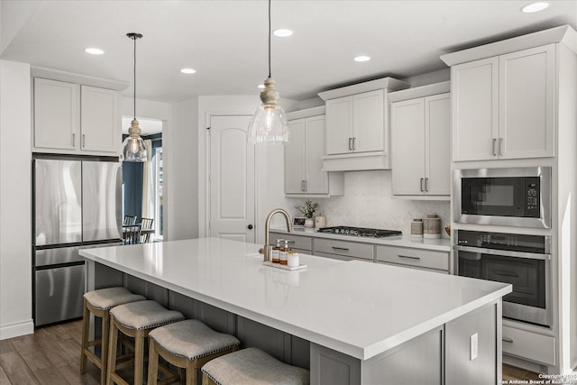 kitchen featuring white cabinets, stainless steel appliances, hanging light fixtures, and an island with sink