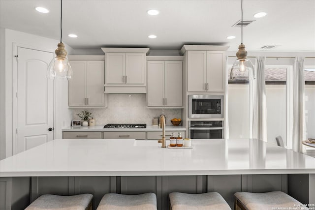 kitchen with a large island with sink, stainless steel appliances, and decorative light fixtures