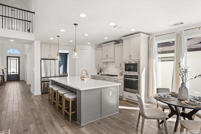 kitchen featuring a kitchen bar, stainless steel appliances, white cabinets, dark hardwood / wood-style floors, and an island with sink