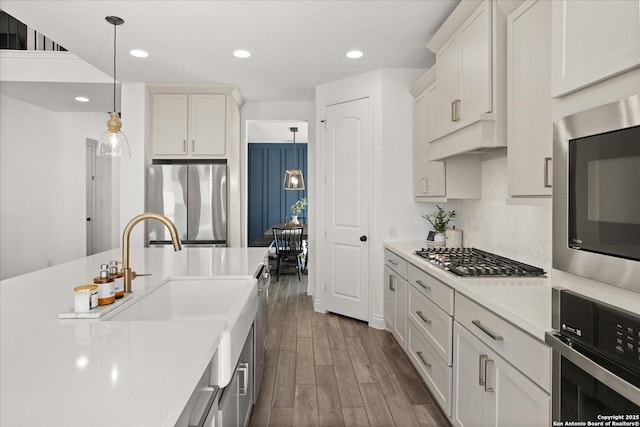 kitchen featuring appliances with stainless steel finishes, white cabinetry, hanging light fixtures, and wood-type flooring