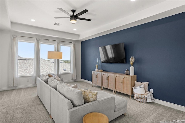 living room featuring a raised ceiling, ceiling fan, and light colored carpet