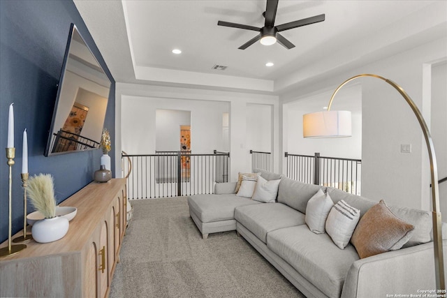 living room featuring a raised ceiling, ceiling fan, and carpet