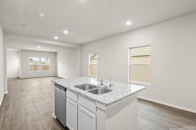 kitchen with light stone counters, stainless steel dishwasher, a kitchen island with sink, sink, and white cabinetry