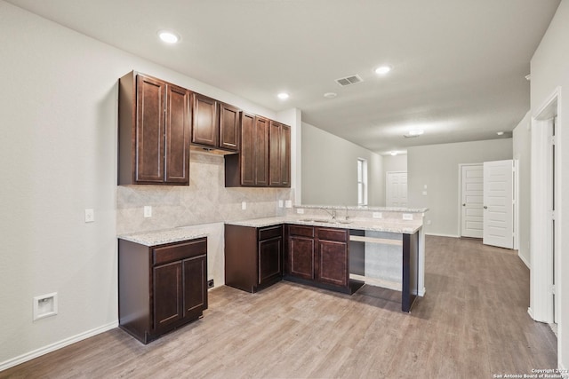 kitchen featuring kitchen peninsula, backsplash, dark brown cabinetry, sink, and light hardwood / wood-style flooring