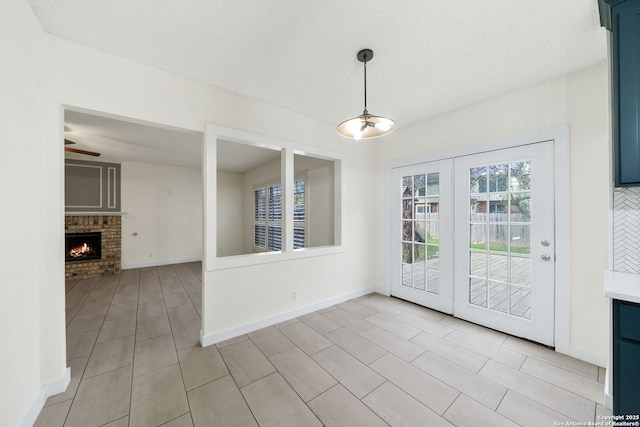 unfurnished dining area featuring a brick fireplace, a textured ceiling, light tile patterned floors, and ceiling fan