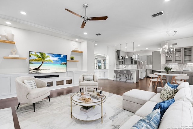 living room featuring crown molding, sink, ceiling fan with notable chandelier, and hardwood / wood-style flooring