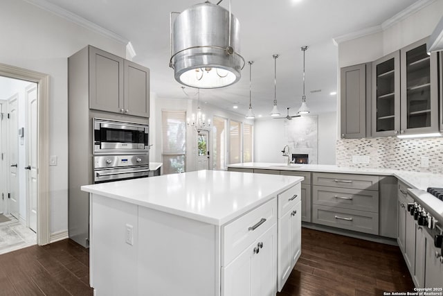 kitchen with a center island, a tile fireplace, appliances with stainless steel finishes, tasteful backsplash, and decorative light fixtures