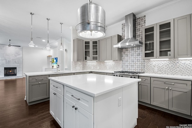 kitchen with gray cabinetry, stainless steel gas stovetop, a center island, and wall chimney range hood