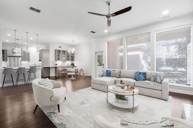 living room featuring ceiling fan with notable chandelier, crown molding, and dark wood-type flooring