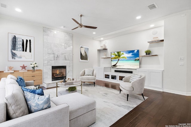 living room with ceiling fan, built in features, crown molding, wood-type flooring, and a fireplace