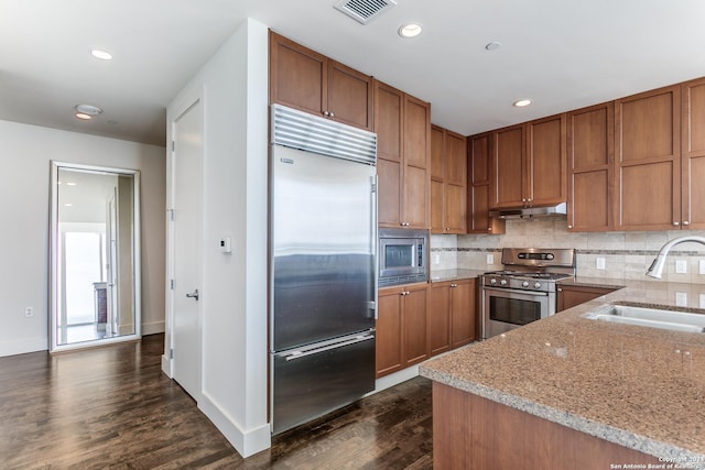 kitchen featuring dark hardwood / wood-style floors, sink, backsplash, built in appliances, and light stone countertops