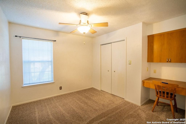 bedroom featuring a textured ceiling, built in desk, a closet, carpet flooring, and ceiling fan