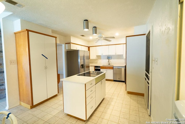 kitchen with a textured ceiling, appliances with stainless steel finishes, a kitchen island, white cabinetry, and ceiling fan