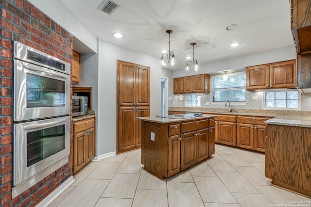 kitchen featuring light stone countertops, appliances with stainless steel finishes, sink, decorative light fixtures, and a kitchen island