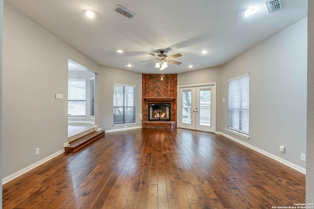 unfurnished living room featuring french doors, a brick fireplace, a textured ceiling, ceiling fan, and dark hardwood / wood-style floors